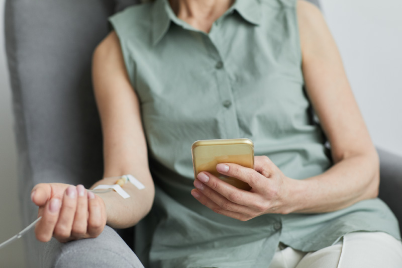 Female patient receiving NAD+ IV therapy while using smartphone in a wellness center.
