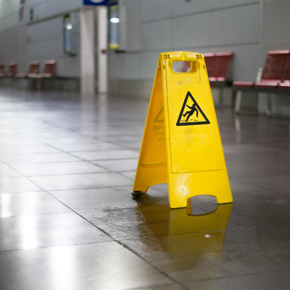 Yellow caution sign on wet floor in a building lobby, warning of slip hazards.